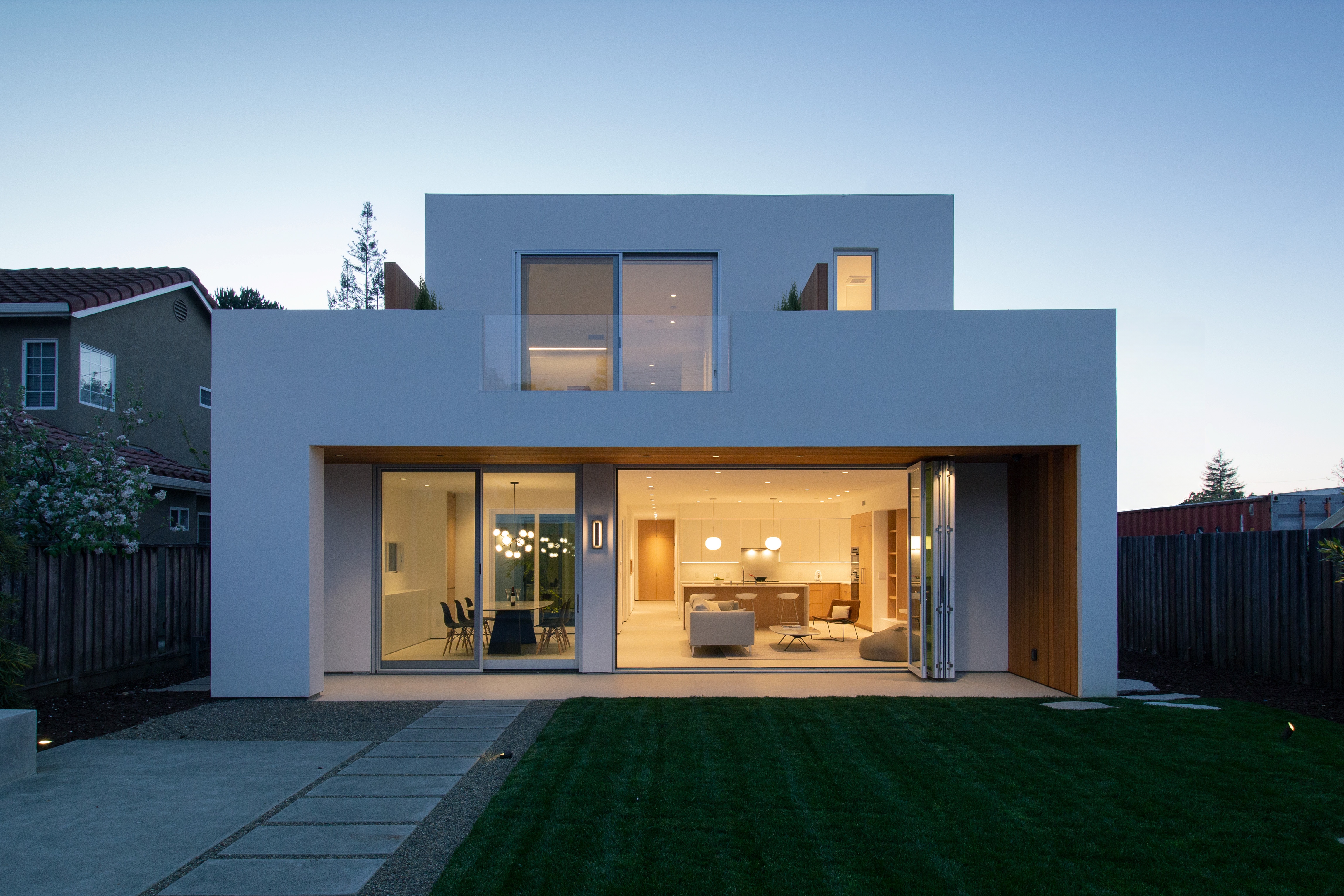 Garden-facing elevation of House of Two Courtyards at dusk, with warm interior light